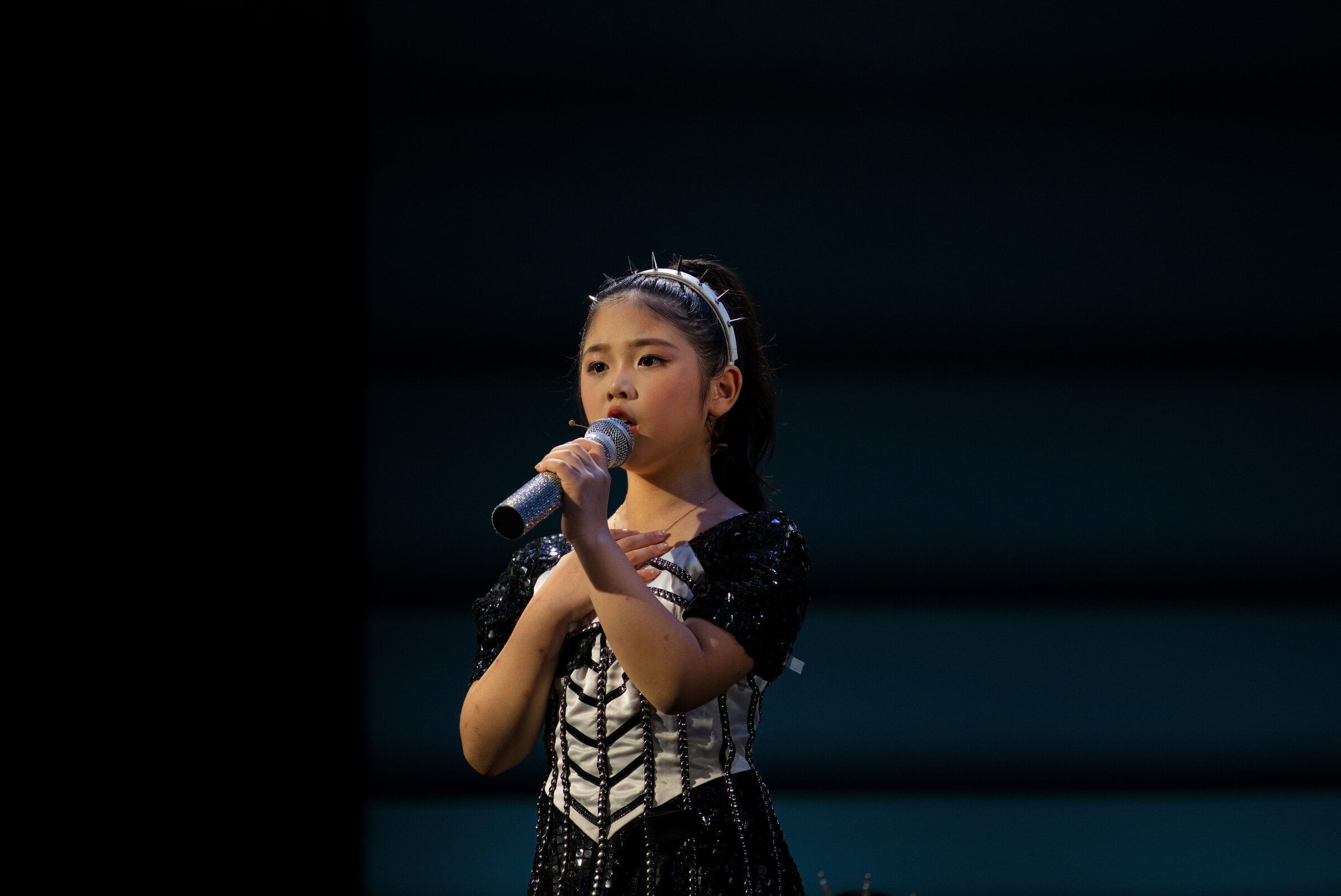 Solo performer in spiked headband singing under spotlight, Six: Teen Edition